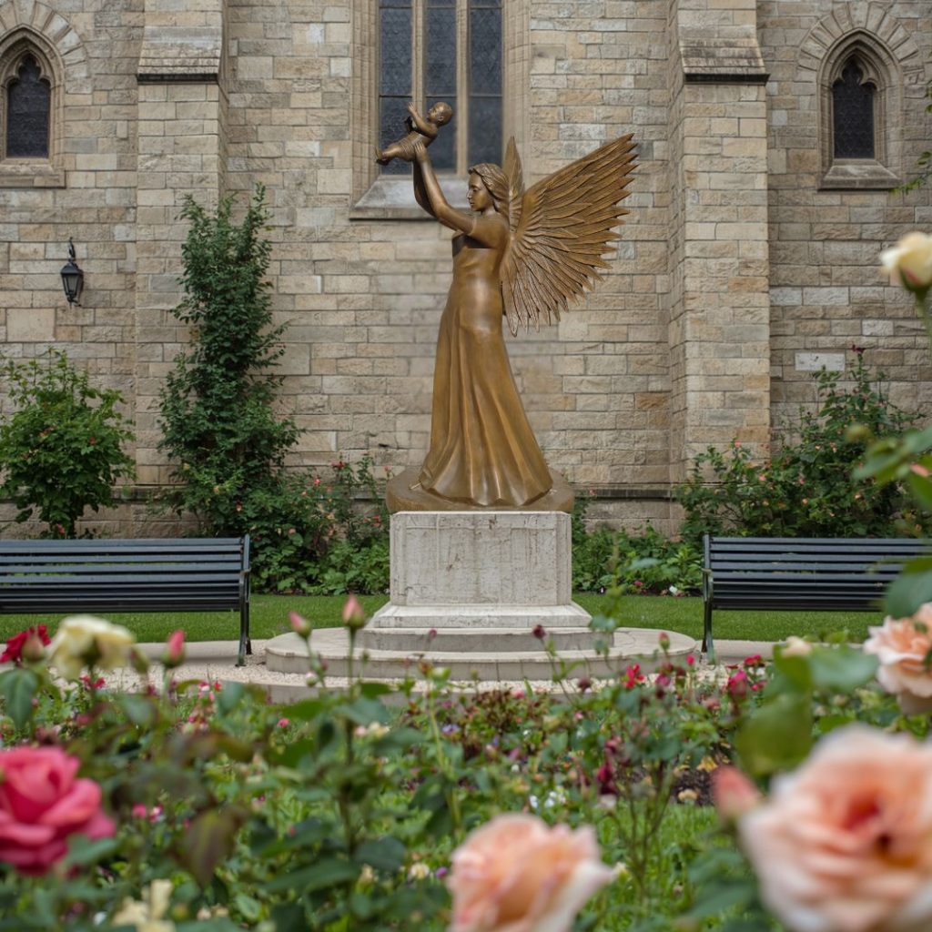 Bronze angel lifting a child in a Catholic memorial garden setting.