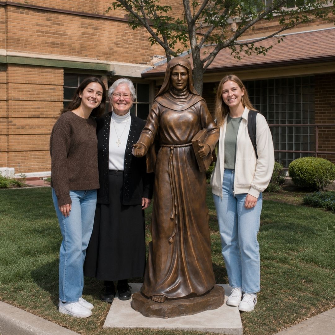 Students and the university chaplain standing beside the St. Clare of Assisi sculpture outside Guardian Angel Hall at the University of St. Francis.